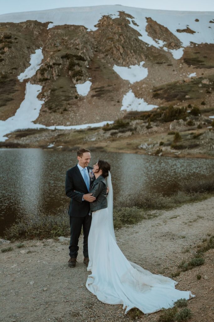 A newlywed couple laughs together by the water's edge during their beautiful Loveland pass lake elopement, surrounded by dramatic alpine tundra.