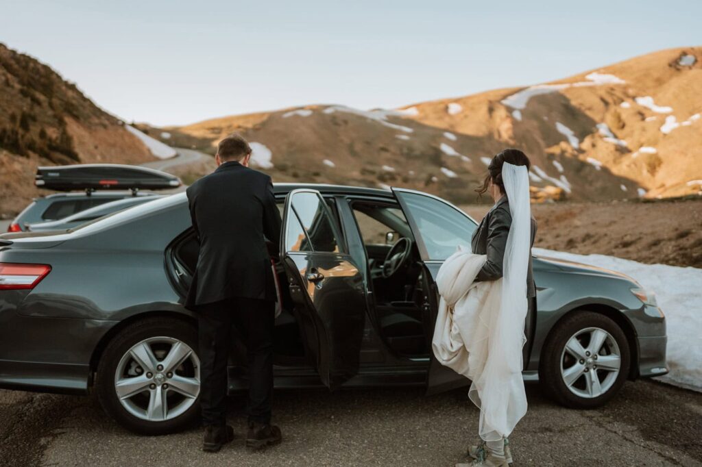 A bride and groom grab their wedding attire from a parked car, preparing for eloping at Loveland Pass right near the mountain trailhead.