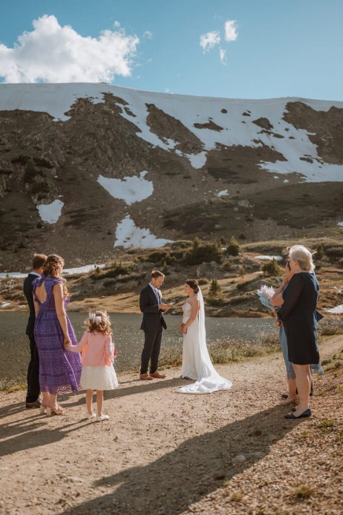 A wide-angle view of an intimate Loveland Pass wedding showing the bride and groom standing by the alpine lake with their small group of family members.