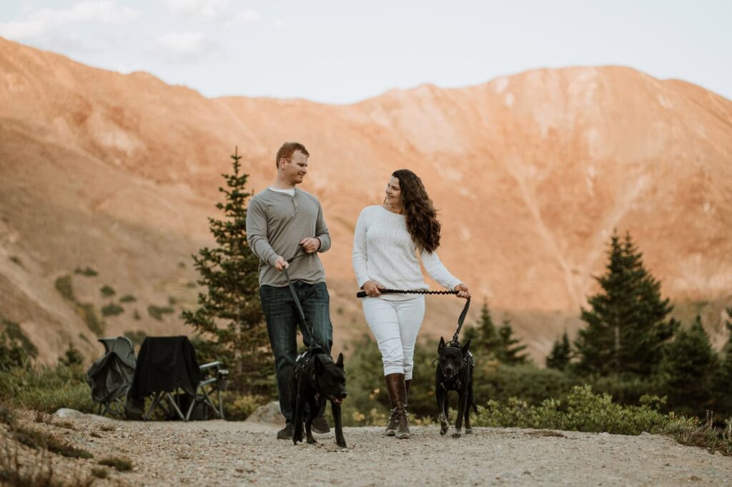 A couple hikes a mountain trail with their two black dogs, showing exactly how stunning Loveland Pass is at sunset for a proposal.