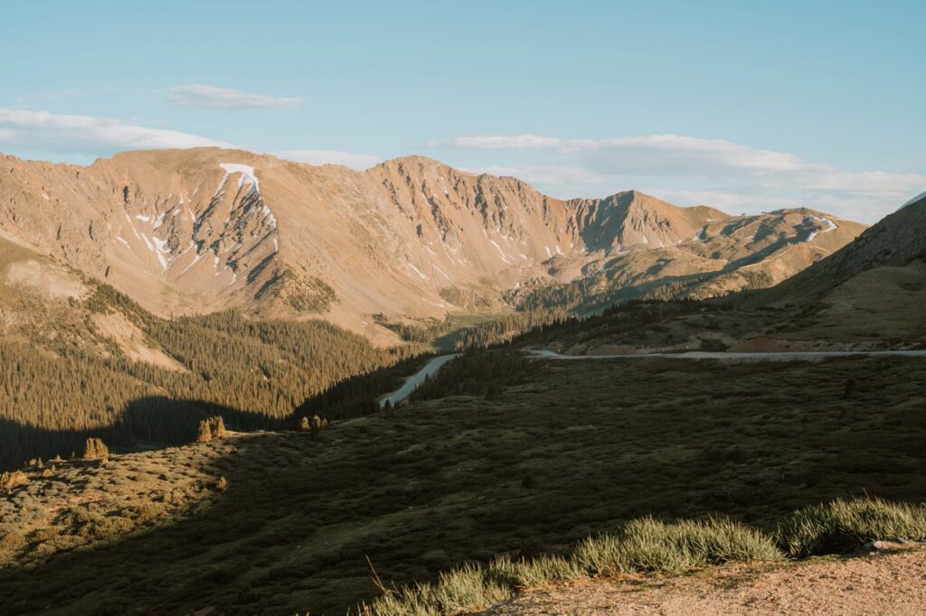 A sweeping landscape view of the winding Loveland pass scenic drive cutting through a deep evergreen valley below sunlit mountain peaks.