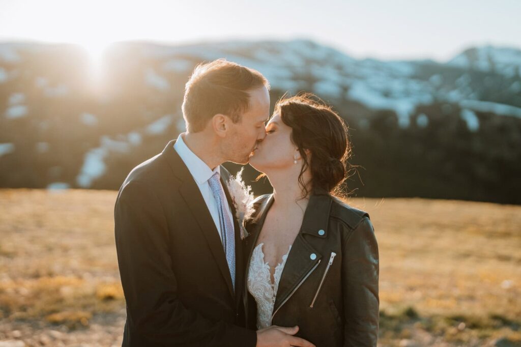 Bright, golden sunset light surrounds a newlywed couple sharing a close kiss at the top of Loveland pass.