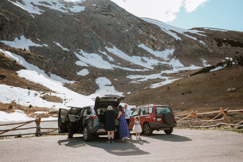 Wedding guests gather their belongings from the trunks of their parked cars near a rustic wooden fence at the parking lot to Loveland Pass Lake.